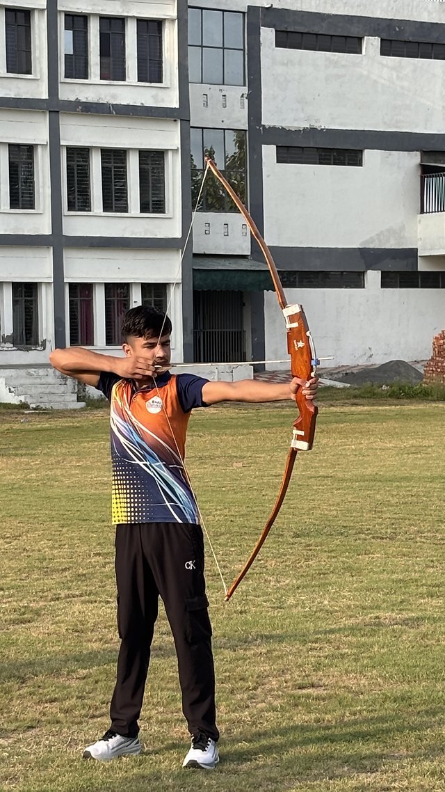 A student at full draw with a bow in front of the academic block