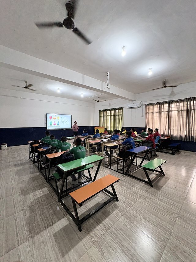 An empty classroom with rows of green and orange desks and a smart display
